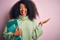 Young african american student woman with afro hair reading books over pink background very happy and excited, winner expression Royalty Free Stock Photo