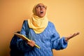 Young African American student woman wearing muslim hijab and backpack holding book crazy and mad shouting and yelling with Royalty Free Stock Photo