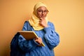 Young African American student woman wearing muslim hijab and backpack holding book looking confident at the camera smiling with Royalty Free Stock Photo