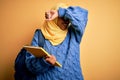 Young African American student woman wearing muslim hijab and backpack holding book Smiling cheerful playing peek a boo with hands