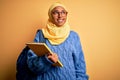 Young African American student woman wearing muslim hijab and backpack holding book smiling looking to the side and staring away Royalty Free Stock Photo