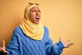 Young African American student woman wearing yellow muslim hijab and sunglasses crazy and mad shouting and yelling with aggressive Royalty Free Stock Photo