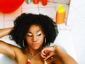 young african-american teen girl laying in bath with foam, wearing swag jewelry flawless, making selfie Royalty Free Stock Photo