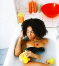 young african-american teen girl laying in bath with foam, wearing swag jewelry flawless, making selfie Royalty Free Stock Photo