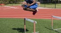 Young African American teenager in the air jumping over a track hurdle on a turf field