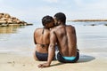 Young african american tourist couple on back view wearing swimwear sitting at the beach Royalty Free Stock Photo