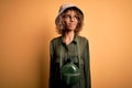 Young african american tourist woman on vacation wearing explorer hat and water canteen smiling looking to the side and staring Royalty Free Stock Photo