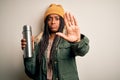 Young african american tourtist woman wearing coat and drinking water from thermo with open hand doing stop sign with serious and Royalty Free Stock Photo