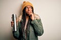 Young african american tourtist woman wearing coat and drinking water from thermo serious face thinking about question, very Royalty Free Stock Photo