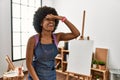 Young african american woman with afro hair at art studio very happy and smiling looking far away with hand over head Royalty Free Stock Photo