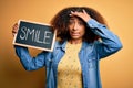 Young african american woman with afro hair holding blackboard with smile message stressed with hand on head, shocked with shame Royalty Free Stock Photo