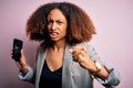 Young african american woman with afro hair holding cracked and broken smartphone screen annoyed and frustrated shouting with