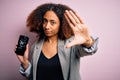 Young african american woman with afro hair holding cracked and broken smartphone screen with open hand doing stop sign with