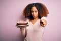 Young african american woman with afro hair holding delicious birthday cake pointing with finger to the camera and to you, hand Royalty Free Stock Photo