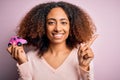 Young african american woman with afro hair holding with hand small pink toy car very happy pointing with hand and finger to the