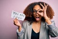 Young african american woman with afro hair holding paper with you are fired message with happy face smiling doing ok sign with Royalty Free Stock Photo