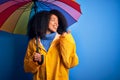 Young african american woman with afro hair under colorful umbrella wearing winter coat for rain pointing and showing with thumb Royalty Free Stock Photo