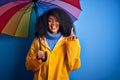 Young african american woman with afro hair under colorful umbrella wearing winter coat for rain surprised with an idea or Royalty Free Stock Photo