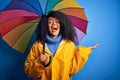 Young african american woman with afro hair under colorful umbrella wearing winter coat for rain very happy and excited, winner Royalty Free Stock Photo