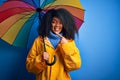 Young african american woman with afro hair under colorful umbrella wearing winter coat for rain very happy pointing with hand and Royalty Free Stock Photo