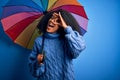 Young african american woman with afro hair under colorful umbrella for winter weather rain with happy face smiling doing ok sign Royalty Free Stock Photo