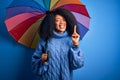 Young african american woman with afro hair under colorful umbrella for winter weather rain surprised with an idea or question Royalty Free Stock Photo