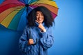 Young african american woman with afro hair under colorful umbrella for winter weather rain very happy pointing with hand and Royalty Free Stock Photo