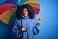 Young african american woman with afro hair under colorful umbrella for winter weather rain very happy pointing with hand and Royalty Free Stock Photo