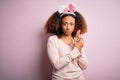 Young african american woman with afro hair wearing bunny ears over pink background Holding symbolic gun with hand gesture, Royalty Free Stock Photo