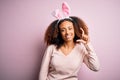 Young african american woman with afro hair wearing bunny ears over pink background smiling and confident gesturing with hand Royalty Free Stock Photo