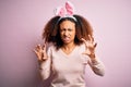 Young african american woman with afro hair wearing bunny ears over pink background smiling funny doing claw gesture as cat, Royalty Free Stock Photo