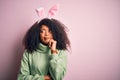 Young african american woman with afro hair wearing easter rabbit ears costume over pink background with hand on chin thinking Royalty Free Stock Photo