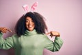 Young african american woman with afro hair wearing easter rabbit ears costume over pink background looking confident with smile Royalty Free Stock Photo