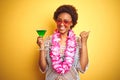 Young african american woman with afro hair wearing flower hawaiian lei and drinking a cocktail pointing and showing with thumb up Royalty Free Stock Photo