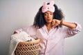 Young african american woman with afro hair wearing pajama doing laundry domestic chores with angry face, negative sign showing