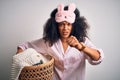 Young african american woman with afro hair wearing pajama doing laundry domestic chores annoyed and frustrated shouting with