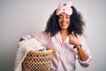 Young african american woman with afro hair wearing pajama doing laundry domestic chores happy with big smile doing ok sign, thumb