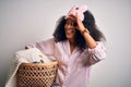 Young african american woman with afro hair wearing pajama doing laundry domestic chores with happy face smiling doing ok sign