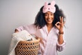 Young african american woman with afro hair wearing pajama doing laundry domestic chores doing ok sign with fingers, excellent