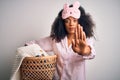Young african american woman with afro hair wearing pajama doing laundry domestic chores with open hand doing stop sign with