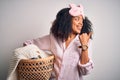 Young african american woman with afro hair wearing pajama doing laundry domestic chores pointing and showing with thumb up to the