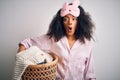 Young african american woman with afro hair wearing pajama doing laundry domestic chores scared in shock with a surprise face,