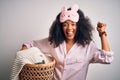 Young african american woman with afro hair wearing pajama doing laundry domestic chores screaming proud and celebrating victory