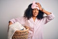 Young african american woman with afro hair wearing pajama doing laundry domestic chores stressed with hand on head, shocked with