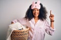 Young african american woman with afro hair wearing pajama doing laundry domestic chores surprised with an idea or question