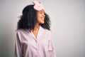 Young african american woman with afro hair wearing sleeping eye mask and pink pajama looking away to side with smile on face, Royalty Free Stock Photo