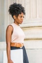 Young African American woman with afro hairstyle, white ear bead pin, wearing sleeveless light color top, dark orange belt, black Royalty Free Stock Photo