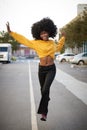 Young African American woman with afro jumps, looking to camera, while crossing street, front view, vertical Royalty Free Stock Photo