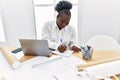 Young african american woman architect using laptop writing on notebook at architecture studio Royalty Free Stock Photo