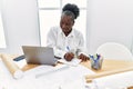 Young african american woman architect using laptop writing on notebook at architecture studio Royalty Free Stock Photo